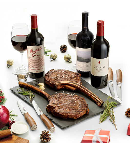Steak on a slate board with wine bottles and glasses on a festive table.