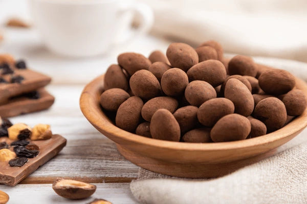 Wooden bowl filled with chocolate-covered almonds on a wooden surface