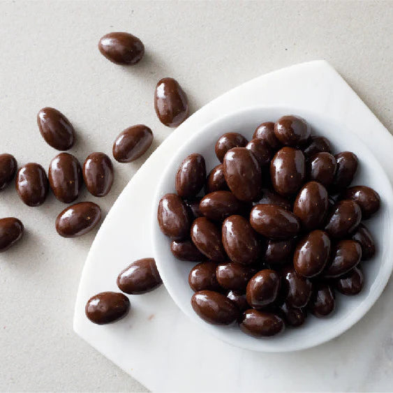 Chocolate-covered almonds in a white bowl on a light gray background
