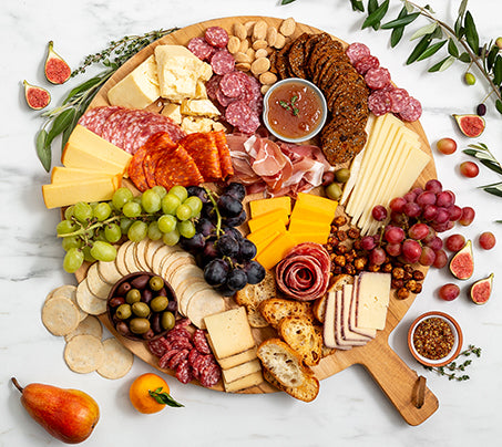 Assorted meats, cheeses, fruits, and crackers on a wooden board with a white background.