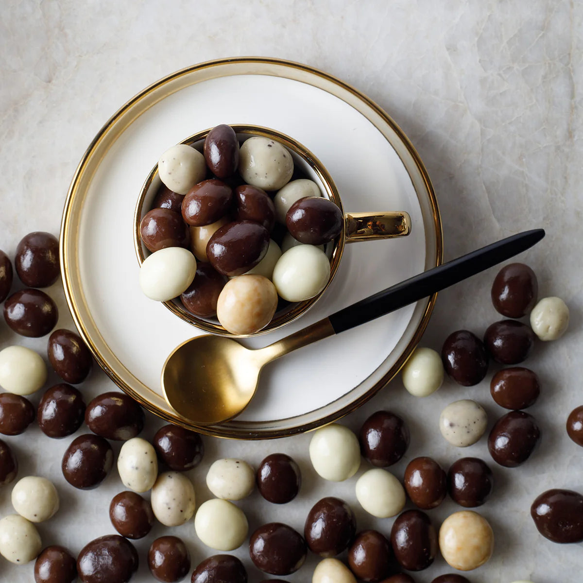 Cup filled with chocolate-covered espresso mix on a plate with a spoon, surrounded by more candies.