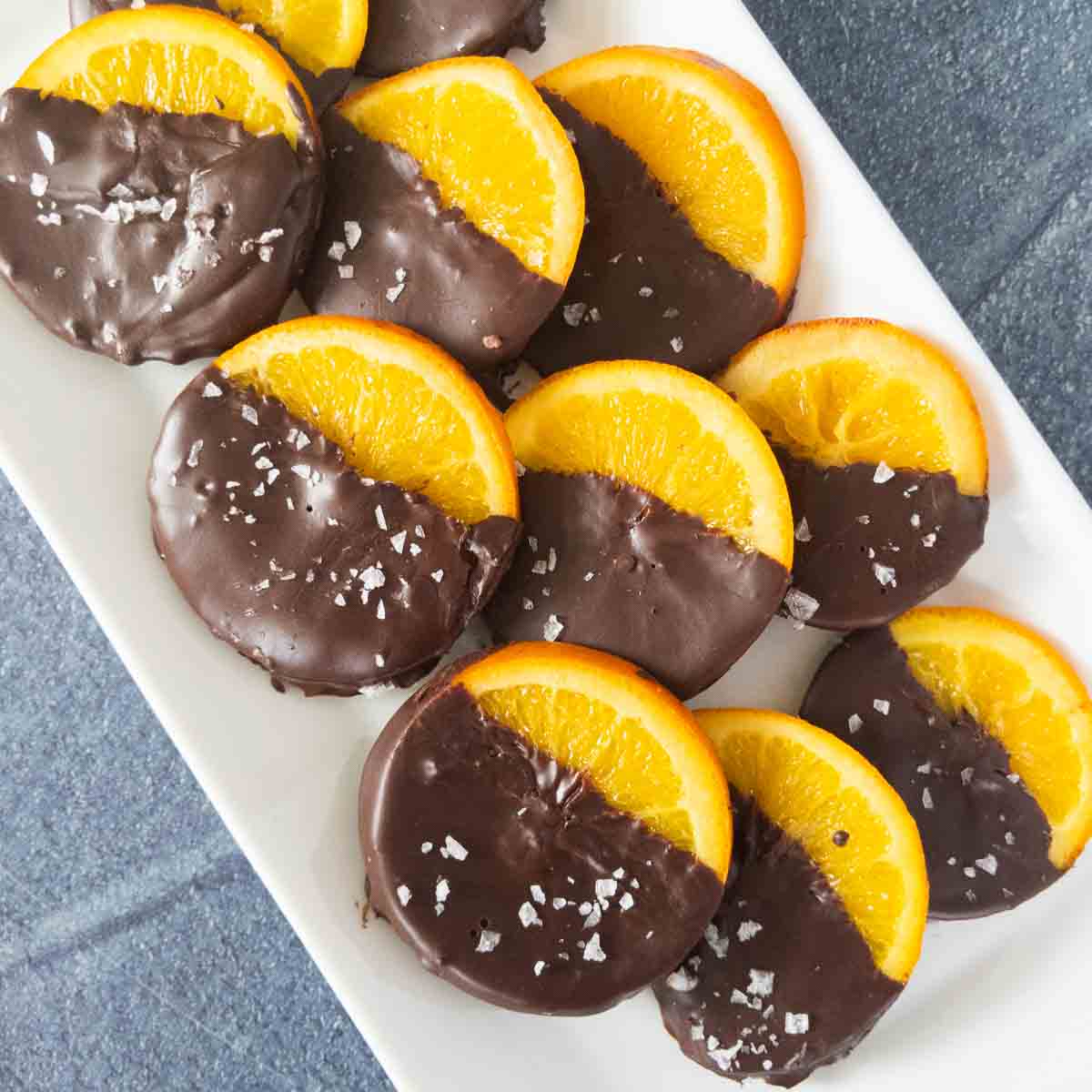 Chocolate-dipped orange slices on a white plate with a gray surface underneath.