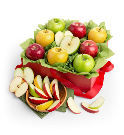 A red gift box filled with red and green apples, green leaves, and a red ribbon, with apple slices arranged on a small wooden plate beside it on a white background.