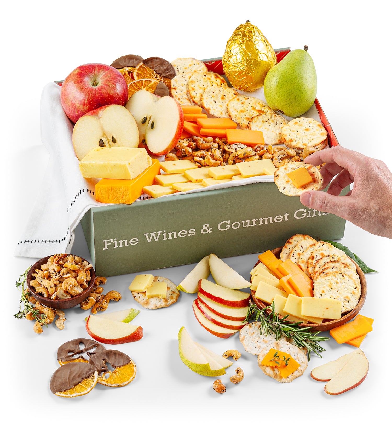 Gourmet gift box with hand reaching in, fruits, cheese, and crackers on a white background.