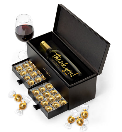 A personalized bottle of wine is shown in a smooth textured handsome gift box with two drawers filled with gold-wrapped truffles.