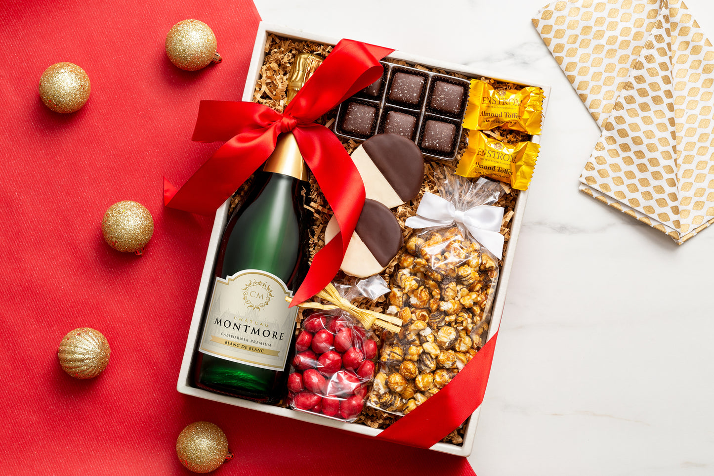 Gift box with Montmore, chocolates, and snacks on a red surface with gold ornaments.