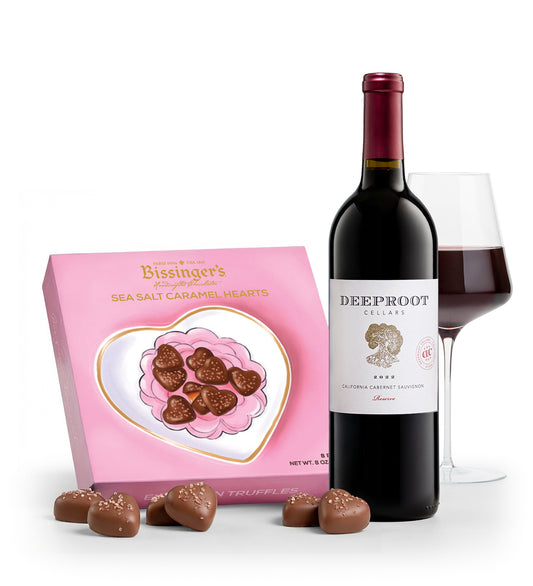Bottle of Deeproot wine with a glass and box of Biseinger's sea salt caramel hearts on a white background