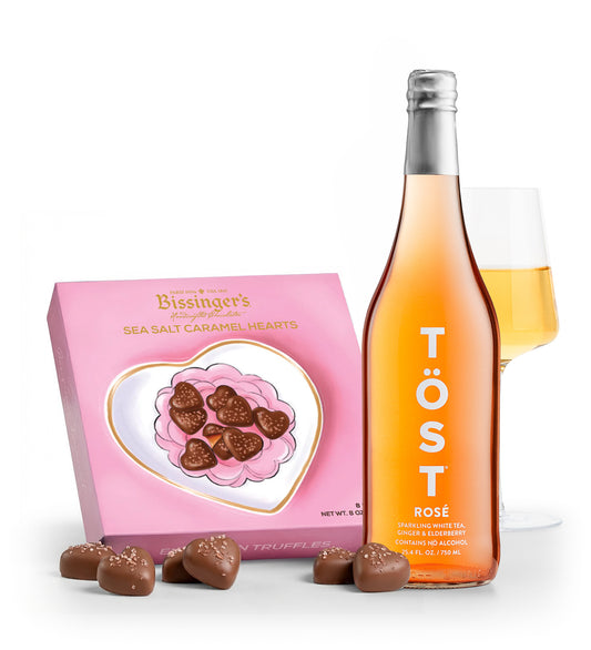 Bottle of Töst Rosé wine with a box of chocolates and a glass of wine on a white background