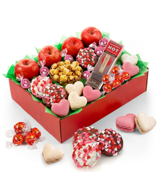 Assorted Valentine's Day treats including cookies, candies, and apples in a box.