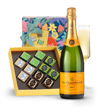 Bottle of Veuve Clicquot champagne with a box of chocolates and a glass of champagne on a white background