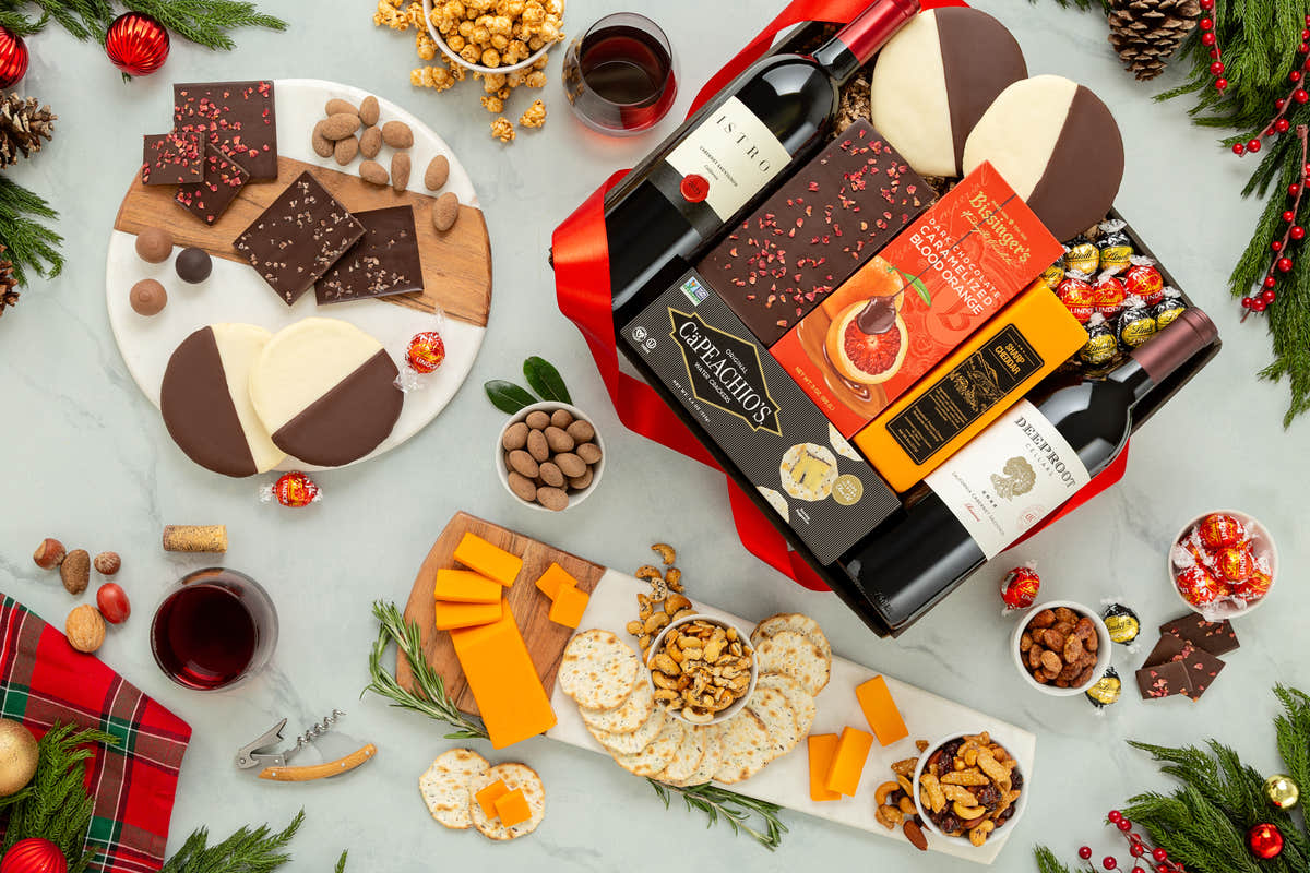 Wine bottles, cheese platter, and assorted snacks on a festive table setting with Christmas decorations.
