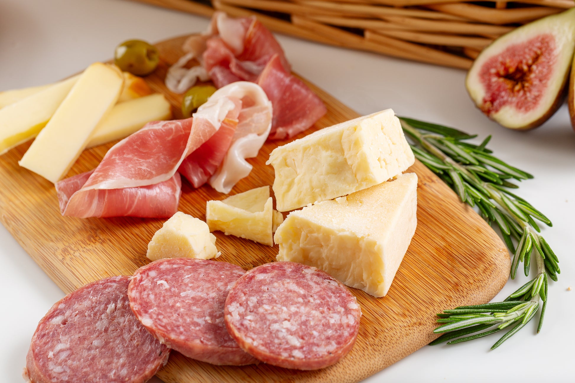 Wooden cutting board with sliced meats, cheeses, and figs on a white surface.