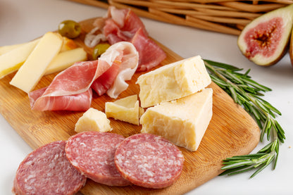 Wooden cutting board with sliced meats, cheeses, and figs on a white surface.