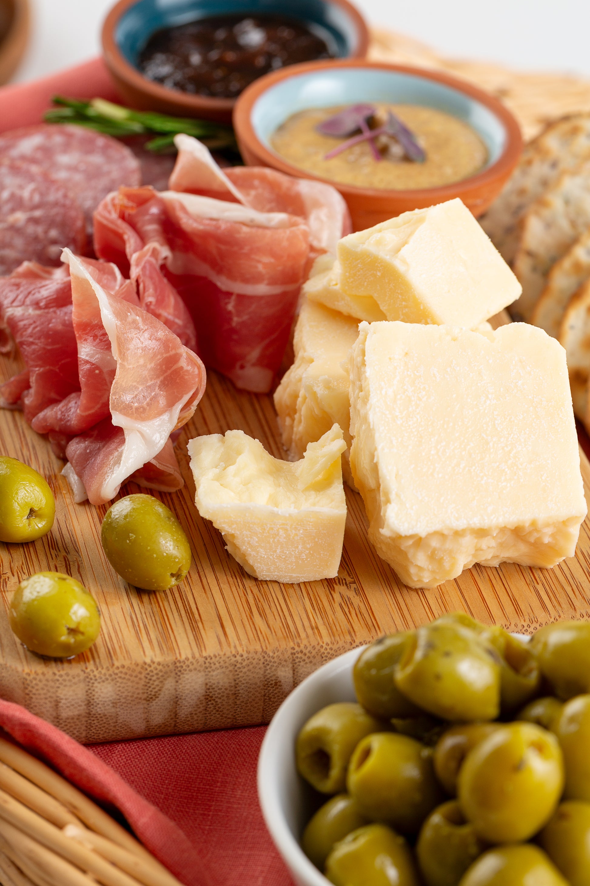 Assorted meats, cheeses, and olives on a wooden board with a red cloth underneath.