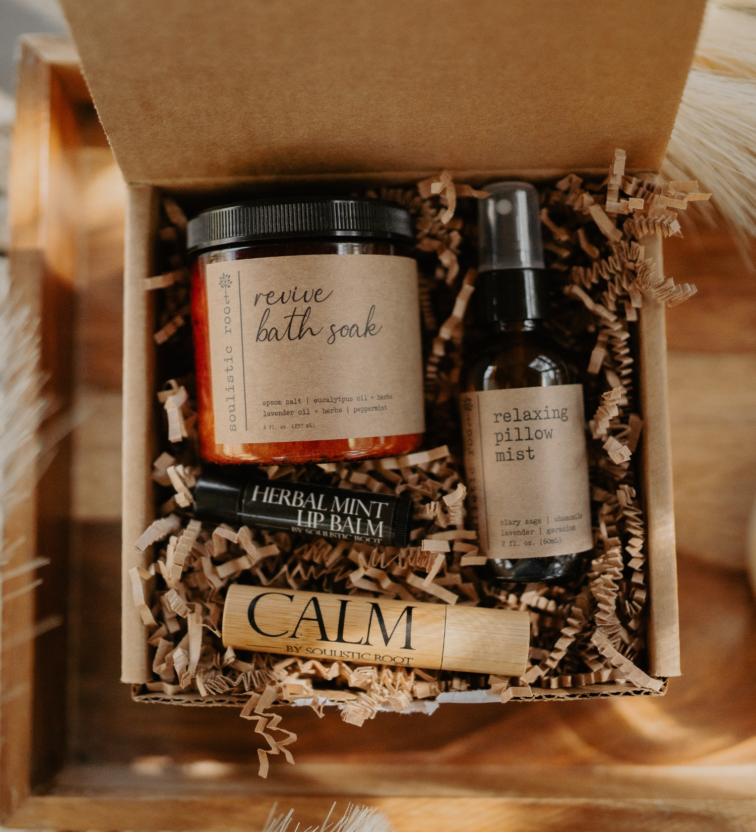 Gift set with bath soak, lip balm, and pillow mist in a box with brown paper lining.