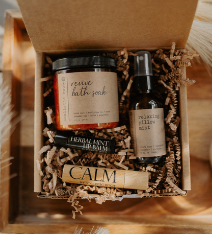 Gift set with bath soak, lip balm, and pillow mist in a box with brown paper lining.