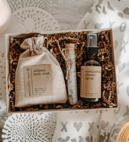 Set of bath and shower products including a bag labeled 'oatmeal bath soak' and a bottle labeled 'eucalyptus shower spray' in a decorative box.