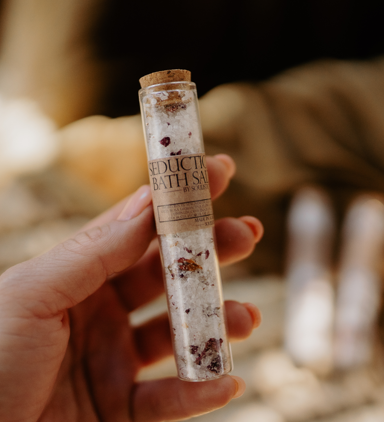 Hand holding a cylindrical container of Rose Bath Salts with a blurred natural background